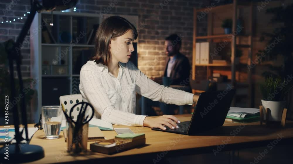 Exhausted girl is working with laptop when manager is bringing more papers at night in dark office, woman is feeling unhappy and stressed. People and job concept. Exhausted girl is working with laptop when manager is bringing more papers at night in dark office, woman is feeling unhappy and stressed. People and job concept.
