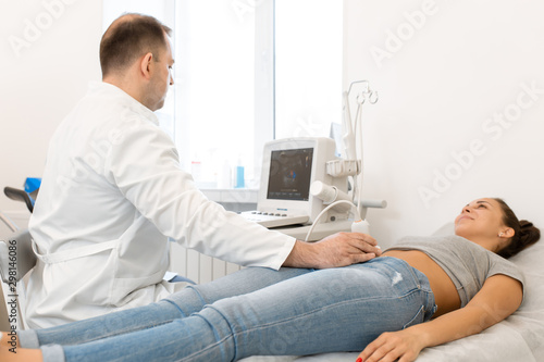 Ultrasound diagnosis of the pelvic organs of the girl. A girl lies on a couch in a white room of ultrasound diagnostics during a diagnostic photo