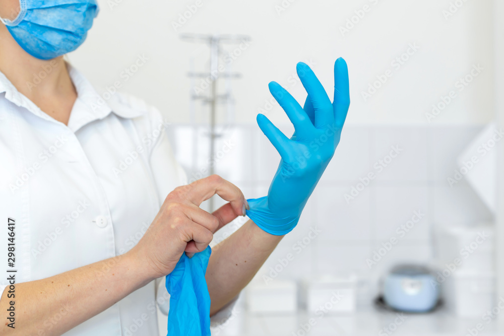 Fototapeta premium A nurse in a white coat puts on rubber gloves before a medical procedure in a bright handling room.