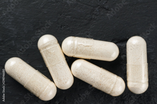 White medical capsules of glucosamine chondroitin, healthy supplement pills on dark background, macro image, top view photo