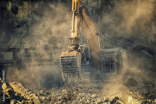 Billede på lærred Heavy machinery surrounded with dust  cloud taking down an old building