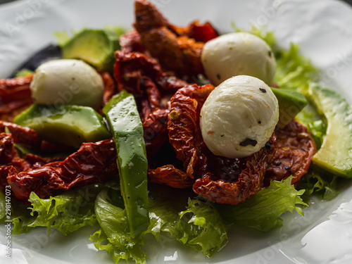 salad made from dried tomatoes, pe-tsai, avocado, and mozzarella cheese. close-up. photo