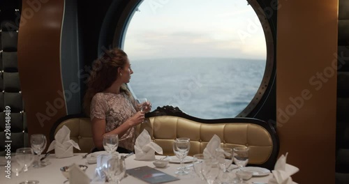 Woman Watching Sunset From window On Luxury Cruise Ship with a glass of winein in restorante. photo