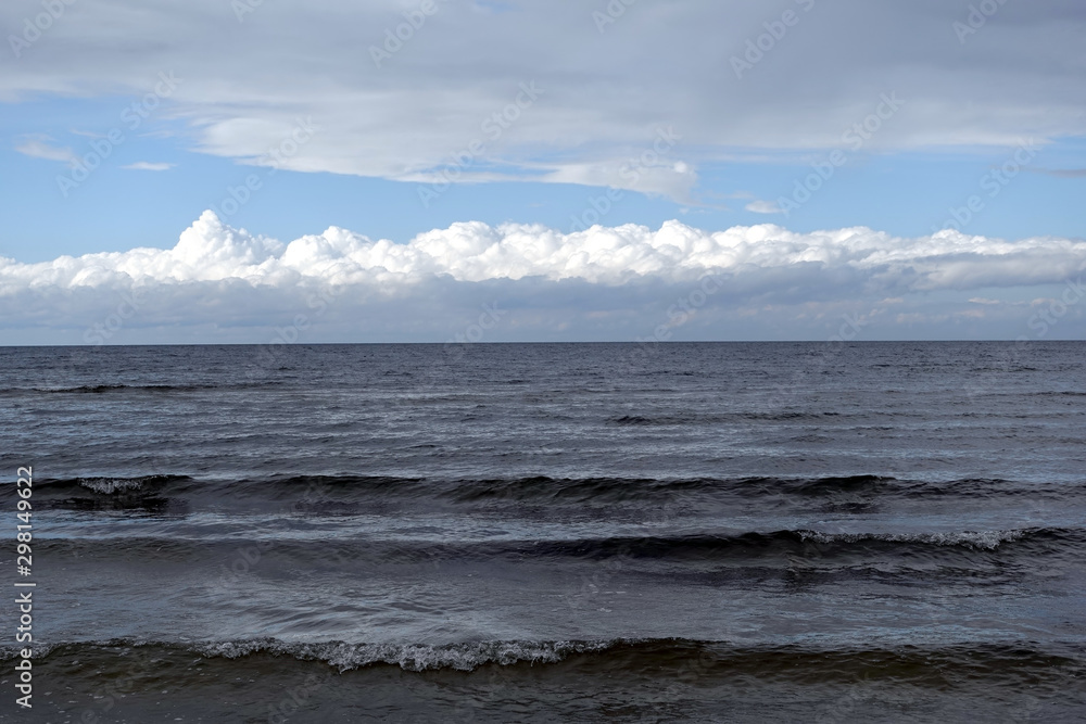 Dark cold waves of the Baltic Sea in the Gulf of Riga in Jurmala with layer of white clouds on skyline on a overcast windy day