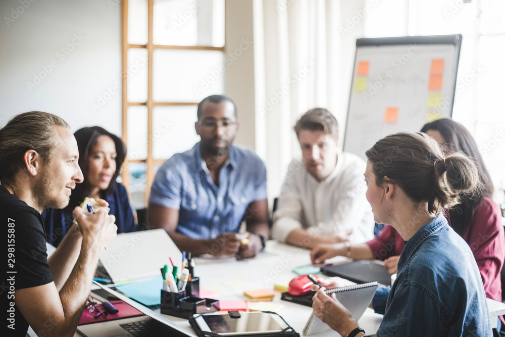 Businesswoman showing diary while explaining business plan to coworkers in meeting at office Businesswoman showing diary while explaining business plan to coworkers in meeting at office