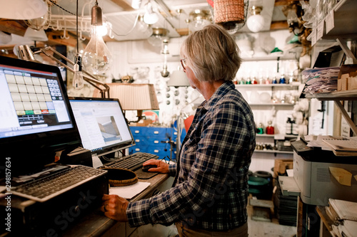 Side view of senior saleswoman using computer while standing at checkout in hardware store photo