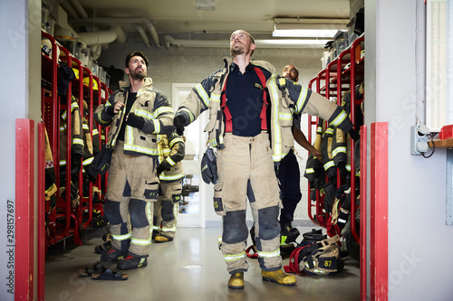 Firefighters looking up while wearing protective workwear in locker room at fire station