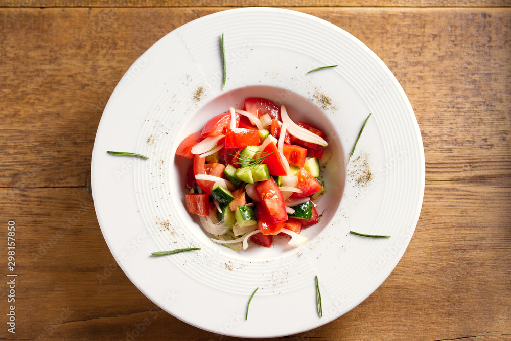 Vegetable salad of fresh tomatoes, cucumbers, bell pepper, onions and herbs in white bowl, wooden table. Overhead, horizontal image Vegetable salad of fresh tomatoes, cucumbers, bell pepper, onions and herbs in white bowl, wooden table. Overhead, horizontal image
