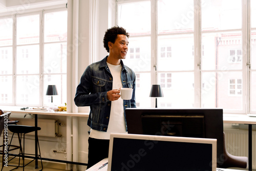 Male executive holding cup while looking away in office photo