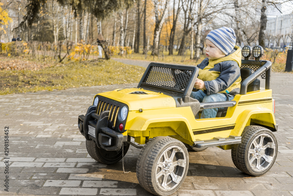 toddler on yellow children drive car with an electric motor in autumn Park