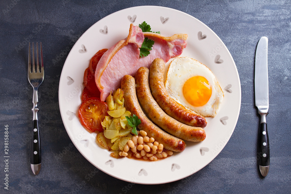 Full English or Irish breakfast with sausages, bacon, egg, tomatoes, fries and beans. Nutritious and healthy morning meal. View from above, top studio shot Full English or Irish breakfast with sausages, bacon, egg, tomatoes, fries and beans. Nutritious and healthy morning meal. View from above, top studio shot