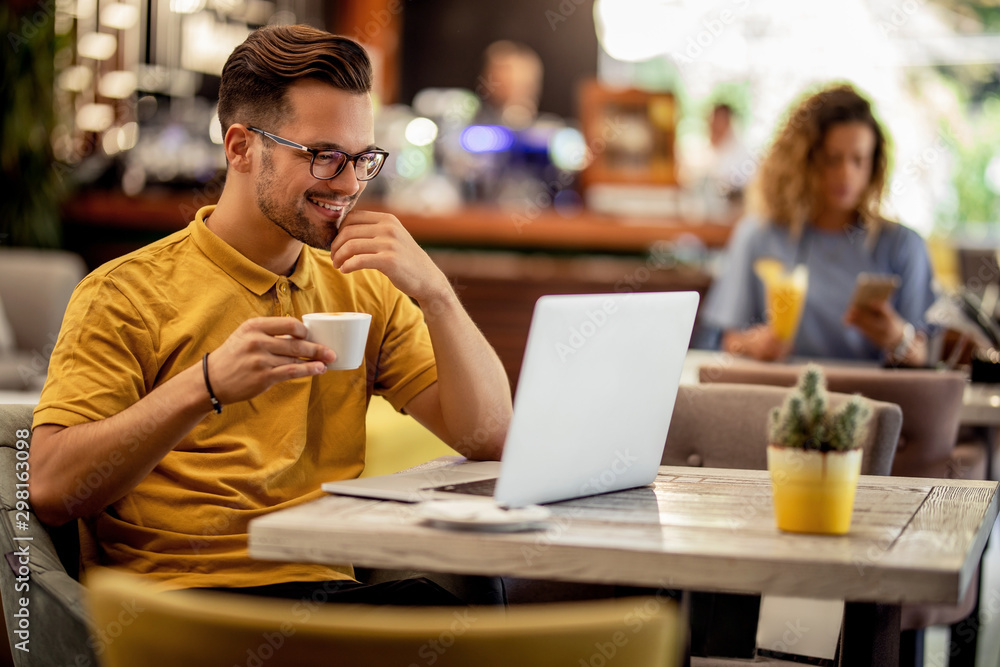 Smiling man reading an e-mail on laptop and drinking coffee in a bar. Smiling man reading an e-mail on laptop and drinking coffee in a bar.