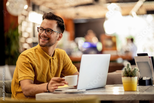 Smiling man enjoying in coffee break while using laptop in a cafe.
