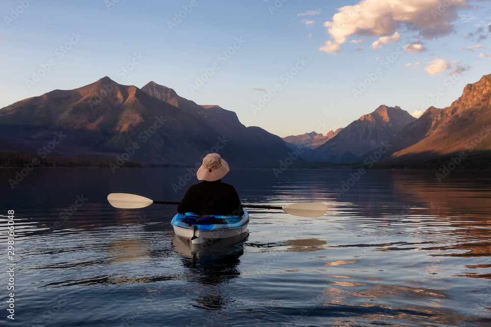 Adventurous Man Kayaking in Lake McDonald during a sunny summer sunset with American Rocky Mountains in the background. Taken in Glacier National Park, Montana, USA.