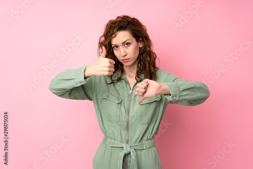 Young pretty woman over isolated pink background making good-bad sign. Undecided between yes or not © luismolinero