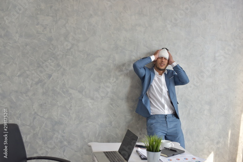 Overworked businessman with bandaged hurt head at workplace with scattered documents 