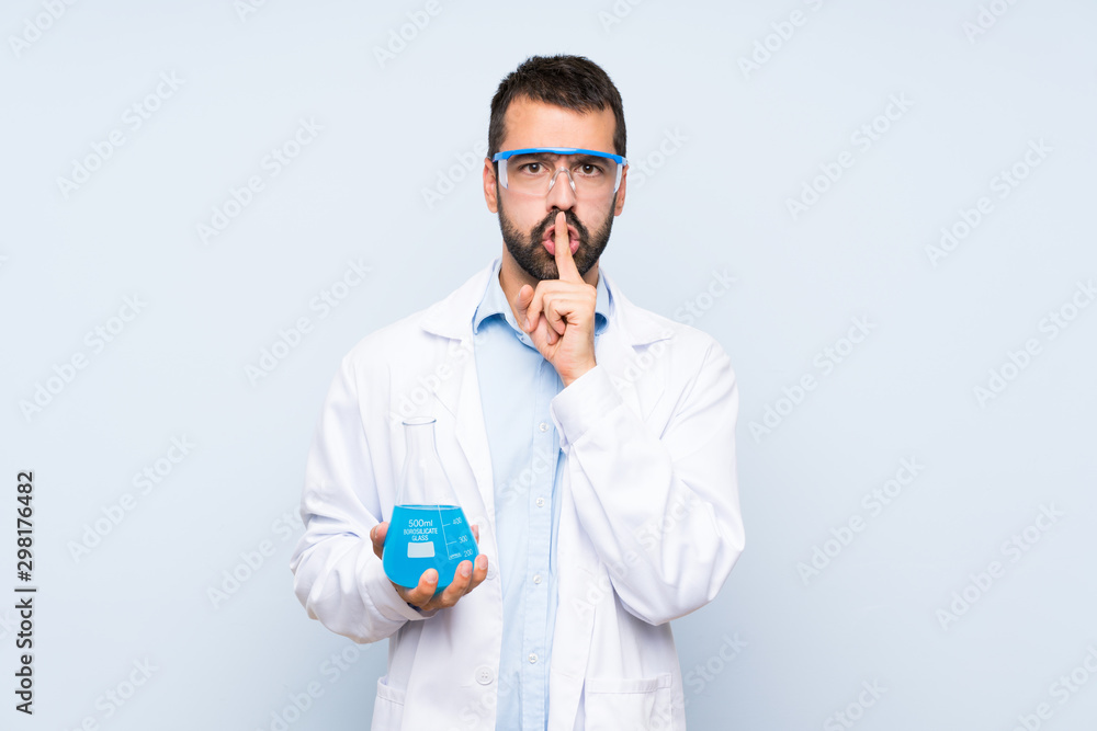 Young scientific holding laboratory flask over isolated background showing a sign of silence gesture putting finger in mouth Young scientific holding laboratory flask over isolated background showing a sign of silence gesture putting finger in mouth