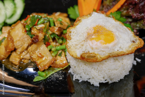 Close up and selected focus view of  Thai spicy Basil with crispy belly pork, Yardlong Bean and red chilli serve with streamed rice and fried egg.