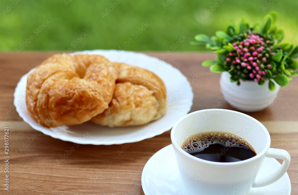 Black coffee with fresh croissant on a wooden table.