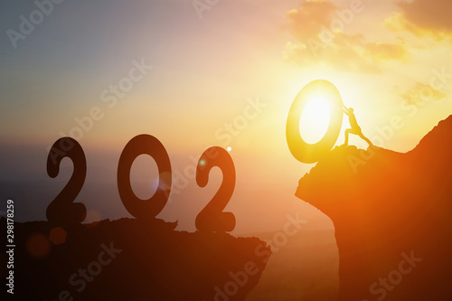 2020 New Year , Young Businessman pushing 2020 New Year towards goals and jump cliff across between active success on silhouette sunset background. Shows about freedom happy new year success concept.