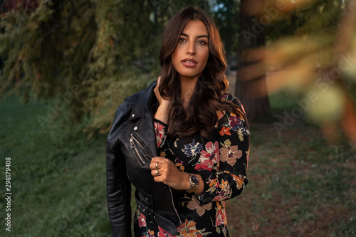 Fashionable gorgeous young woman in floral dress posing with leather jacket in nature 