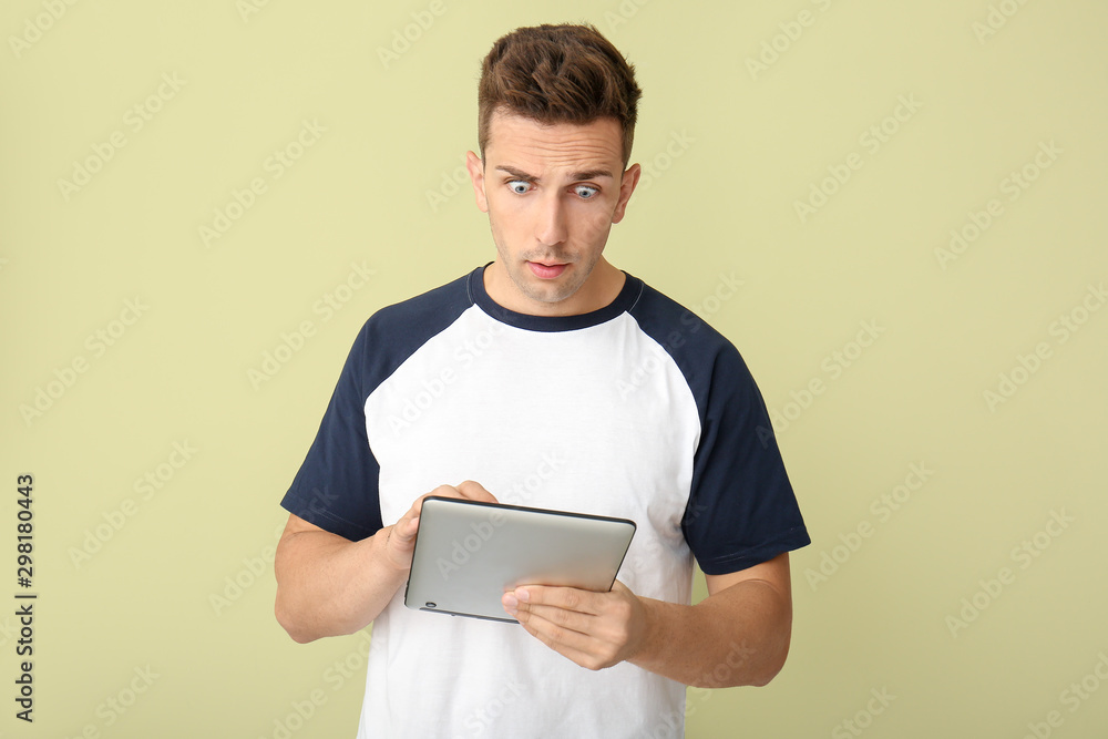 Shocked young man with tablet computer on color background Shocked young man with tablet computer on color background
