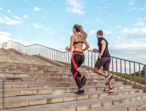 Fototapeta Naklejka Na Ścianę i Meble -  Young athletic couple man woman, jogging stairs morning, summer city, sportswear. Workout athletics, afternoon running. Active fitness lifestyle. Strength motivation. Free space text, view from rear.