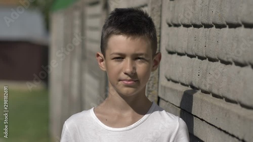 portrait of a funny boy outdoors near the fence stands and looks at the camera in the country photo