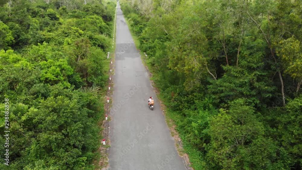 Aerial: couple riding scooter inland Cat Ba island, travel destination in Vietnam. Two people driving motorbike on road through lush green jungle and karst mountain range. Traveling adventures. Aerial: couple riding scooter inland Cat Ba island, travel destination in Vietnam. Two people driving motorbike on road through lush green jungle and karst mountain range. Traveling adventures.