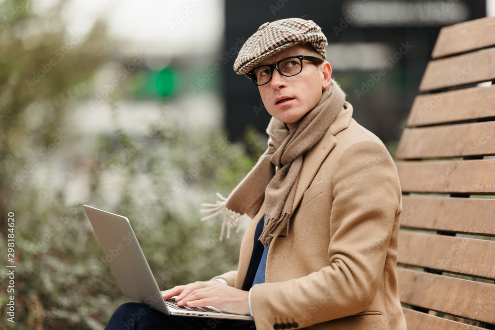 An adult business man sits with a laptop in the Park on a bench and reflects on a new project