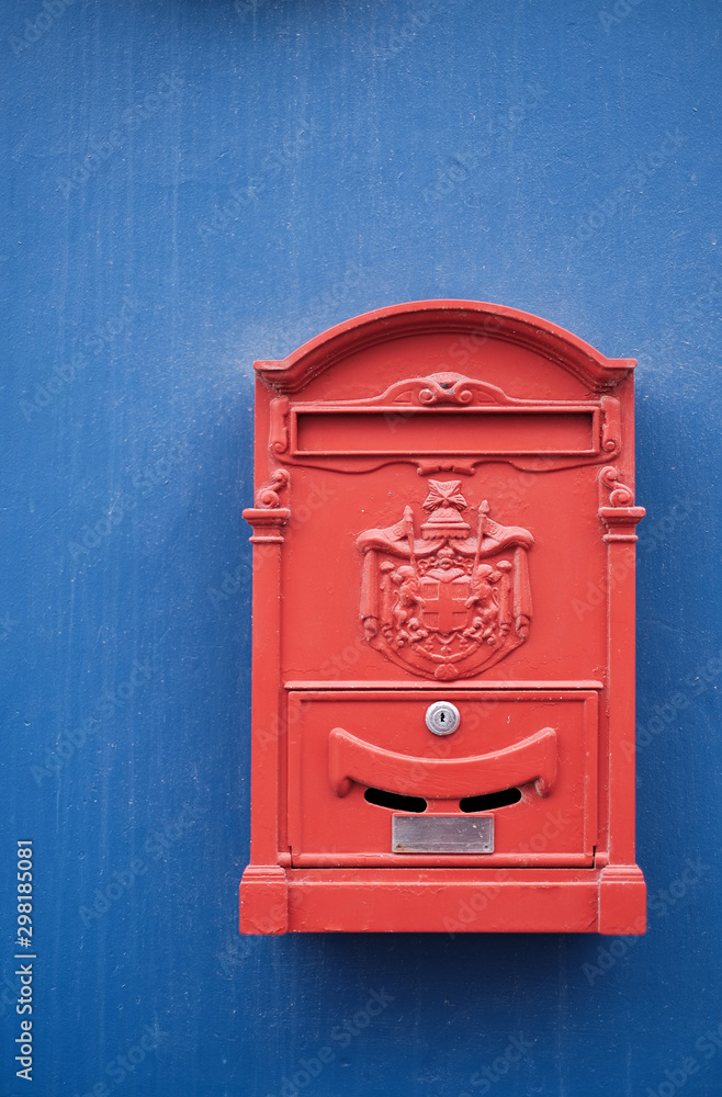 Perfect red letter box on a plain blue wall surface.