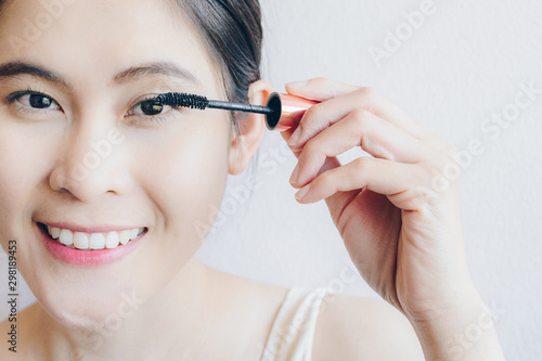 Closeup of young Asian woman applying black mascara on her eyelashes with makeup brush. Mascara is a cosmetic commonly used to enhance the eyelashes.