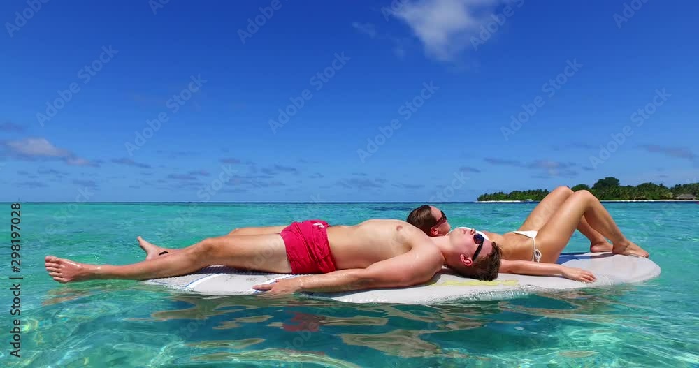 athletic couple relaxing during honeymoon holiday in the Caribbean laying on SUP surfboard athletic couple relaxing during honeymoon holiday in the Caribbean laying on SUP surfboard