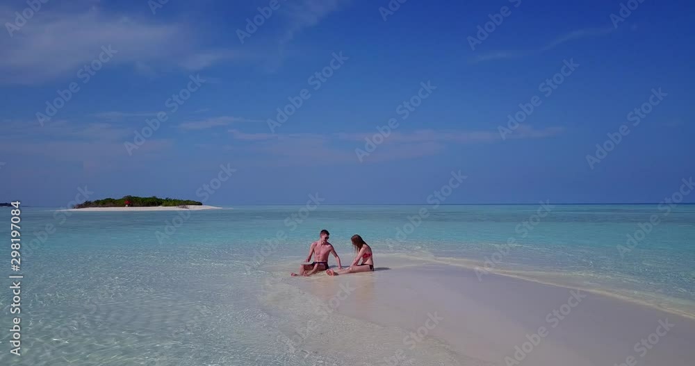 Sweet young couple relaxing off the shore of tiny tropical island sitting on strip of sand Sweet young couple relaxing off the shore of tiny tropical island sitting on strip of sand
