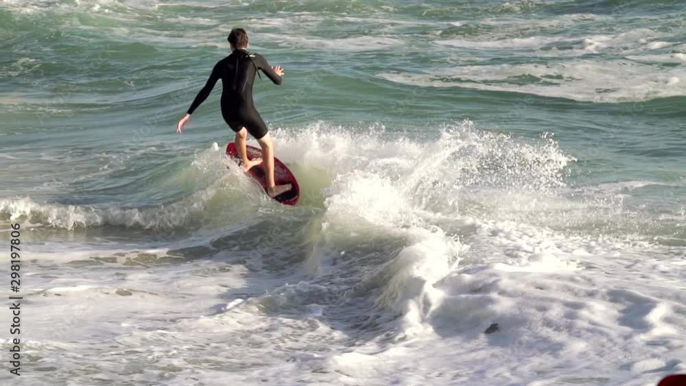 Young skimboarder surfer riding into a wave in slow motion at the beach during sunset Young skimboarder surfer riding into a wave in slow motion at the beach during sunset
