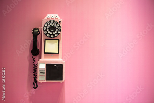 Old vintage phone hanging on a pink wall with copy space