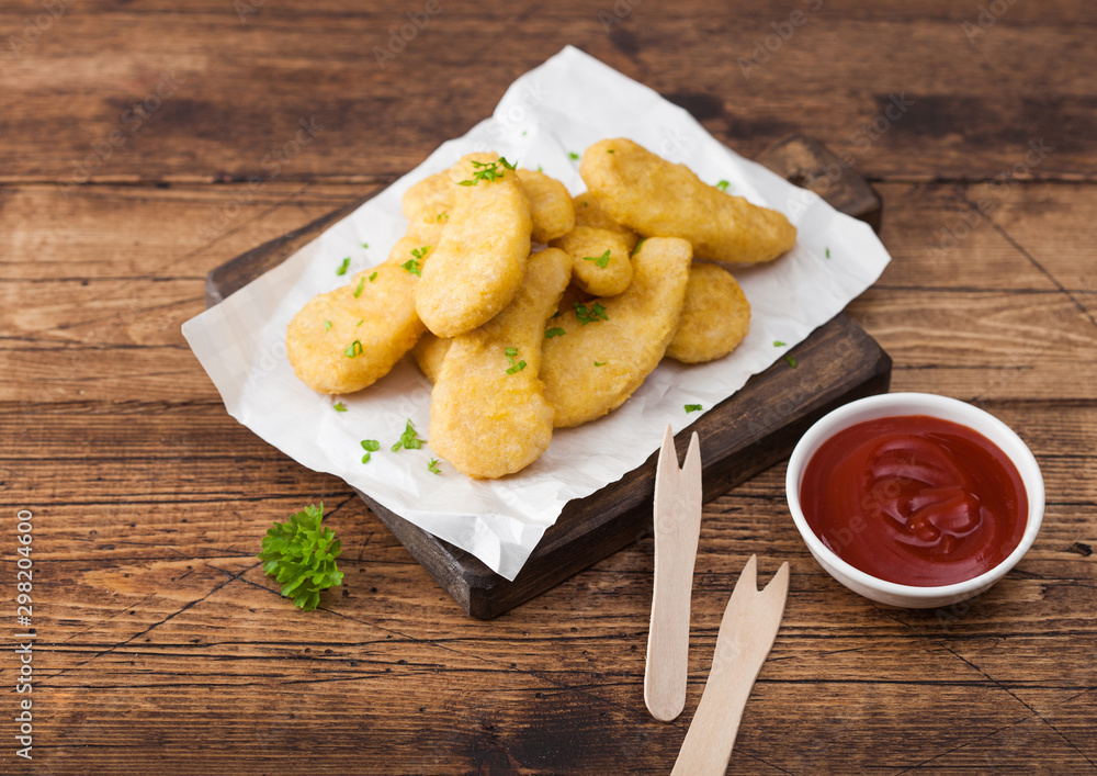 Buttered chicken nuggets on chopping board with wooden forks and ketchup on wooden background. Buttered chicken nuggets on chopping board with wooden forks and ketchup on wooden background.