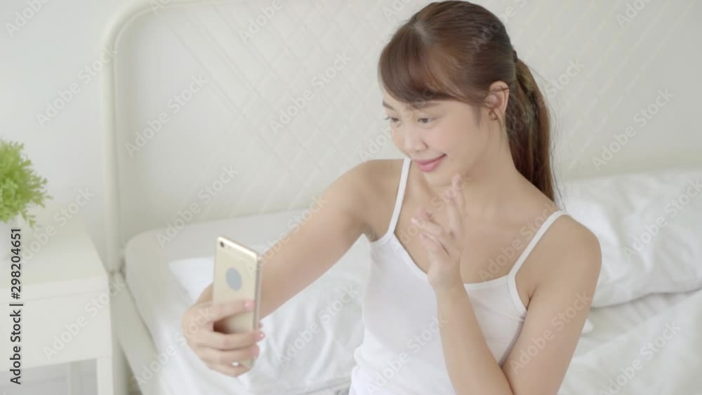 Beautiful portrait young asian woman sitting taking a selfie with smart mobile phone on bedroom in the morning at home, girl is photographing happy and smile with fun, lifestyle concept, slow motion. Beautiful portrait young asian woman sitting taking a selfie with smart mobile phone on bedroom in the morning at home, girl is photographing happy and smile with fun, lifestyle concept, slow motion.