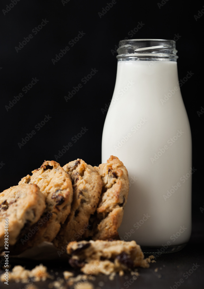 Homemade organic oatmeal cookies with raisins and apricots and bottle of milk on dark wooden background. Homemade organic oatmeal cookies with raisins and apricots and bottle of milk on dark wooden background.
