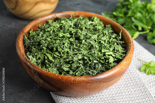 Wooden bowl of dried parsley on table, closeup