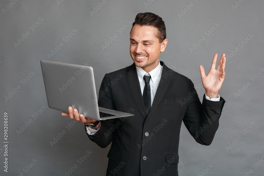 Businessman studio standing isolated on grey video chatting on laptop waving cheerful Businessman studio standing isolated on grey video chatting on laptop waving cheerful