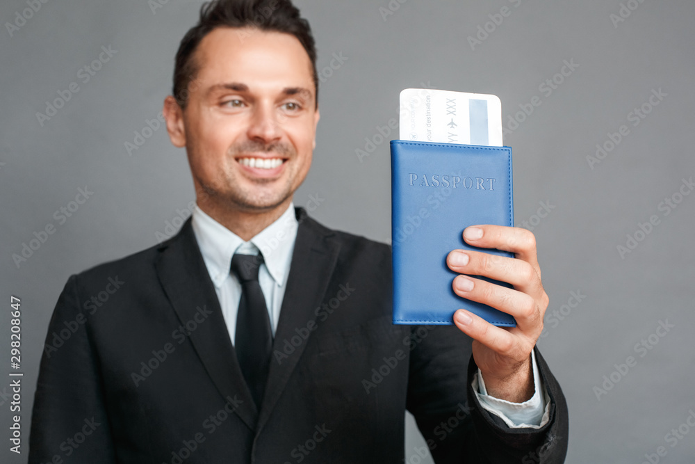 Businessman studio standing isolated on grey with passport and ticket close-up cheerful blurred background Businessman studio standing isolated on grey with passport and ticket close-up cheerful blurred background