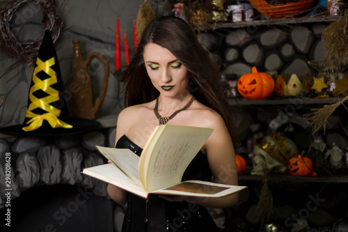 A beautiful, young witch in a black corset with a book in his hands, conjures, reads a spell. Studio photo. Girl in costume on halloween. A model with clean skin.