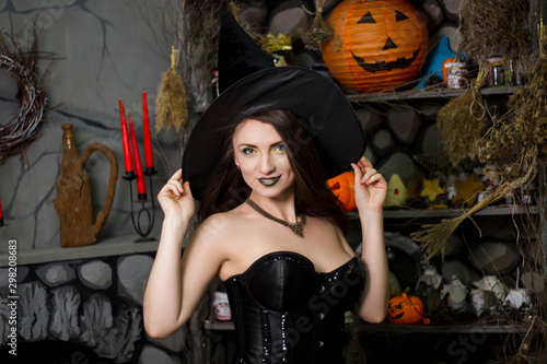 A beautiful, young girl in a black corset, a green skirt and a black hat. The image of a witch in halloween. A model with clean skin.