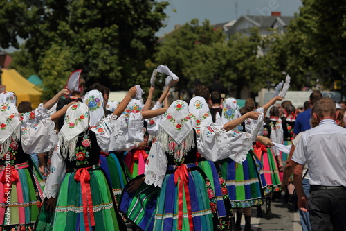 group of people at the festival, in regional folk costumes from Lowicz region, girls walk in street waving handkerchief