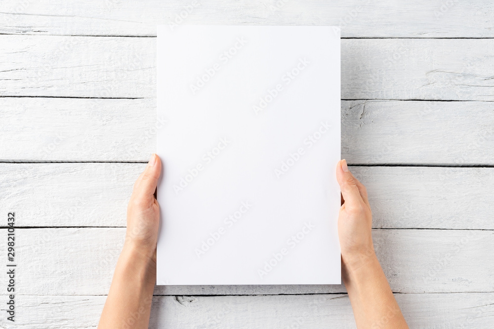 Female hands holding empty paper sheet on white wooden background. Top view Female hands holding empty paper sheet on white wooden background. Top view