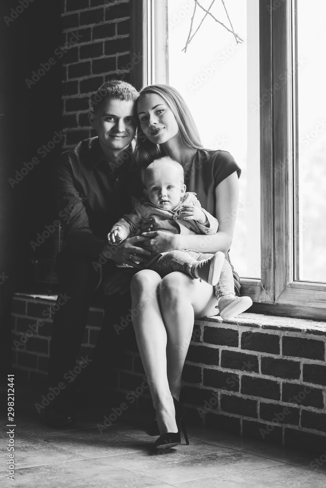 Naklejka premium Parents and their child sitting at the window. Mom, dad and baby. Portrait of young family. Happy family life. Man was born.