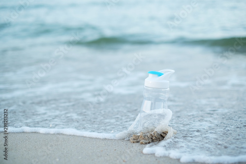 The reusable water plastic bottle on the beach with sea and sand background.Selected focus. Save the world and sea life concept by use the reusable water bottle for to reduce the plastic waste.