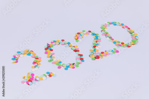 Side view of an inscription of number 2020 new year made of multicolored confetti on a white background