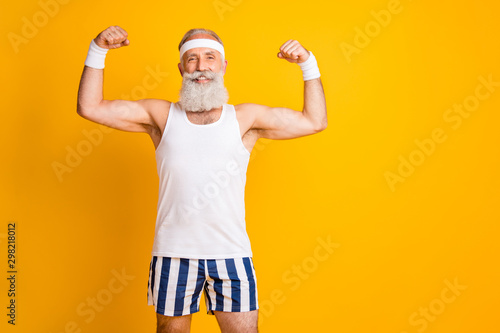 Fototapeta Naklejka Na Ścianę i Meble -  Photo of handsome cheerful positive man old smiling toothily demonstrating biceps near empty space isolated vivid yellow color background